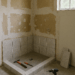 Half-finished bathroom with exposed drywall and scattered tools symbolizing broken promises in home repair