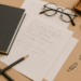 A cozy writer’s desk with scattered pages, pencils, eyeglasses, a coffee-colored notebook, and paperclips in warm natural light — capturing the creative chaos of writing a personal story.